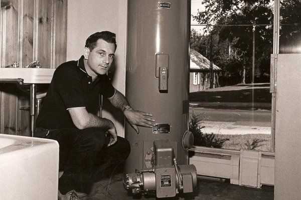 A technician installing a water heater, 1960s